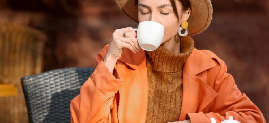 A woman sitting at an outdoor cafe table sipping from a mug